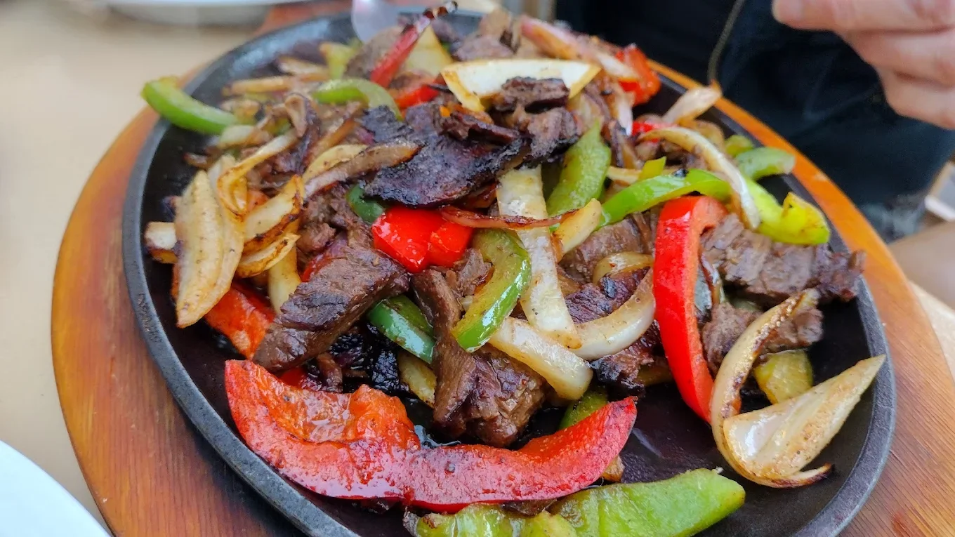 Fajitas Texanas - Sizzling strips of grilled steak or chicken served on a cast-iron skillet with peppers, onions, warm tortillas, and all the fixings.